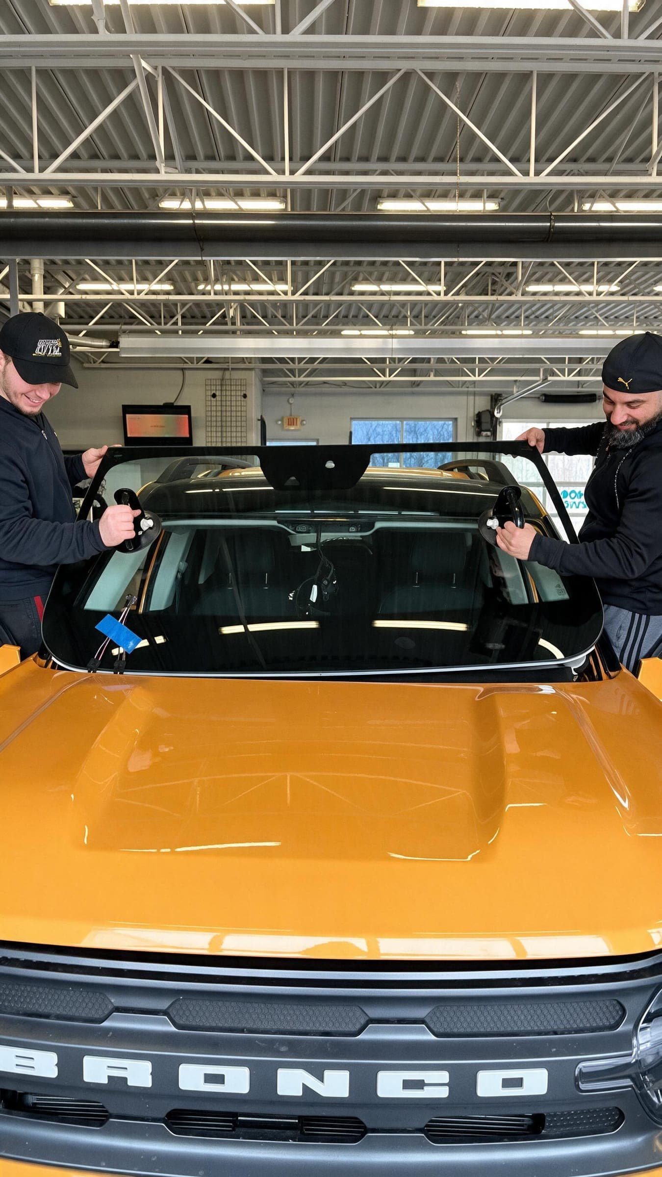 Two Win City Auto Glass technicians setting a new windshield on a Ford Bronco in the Windsor shop